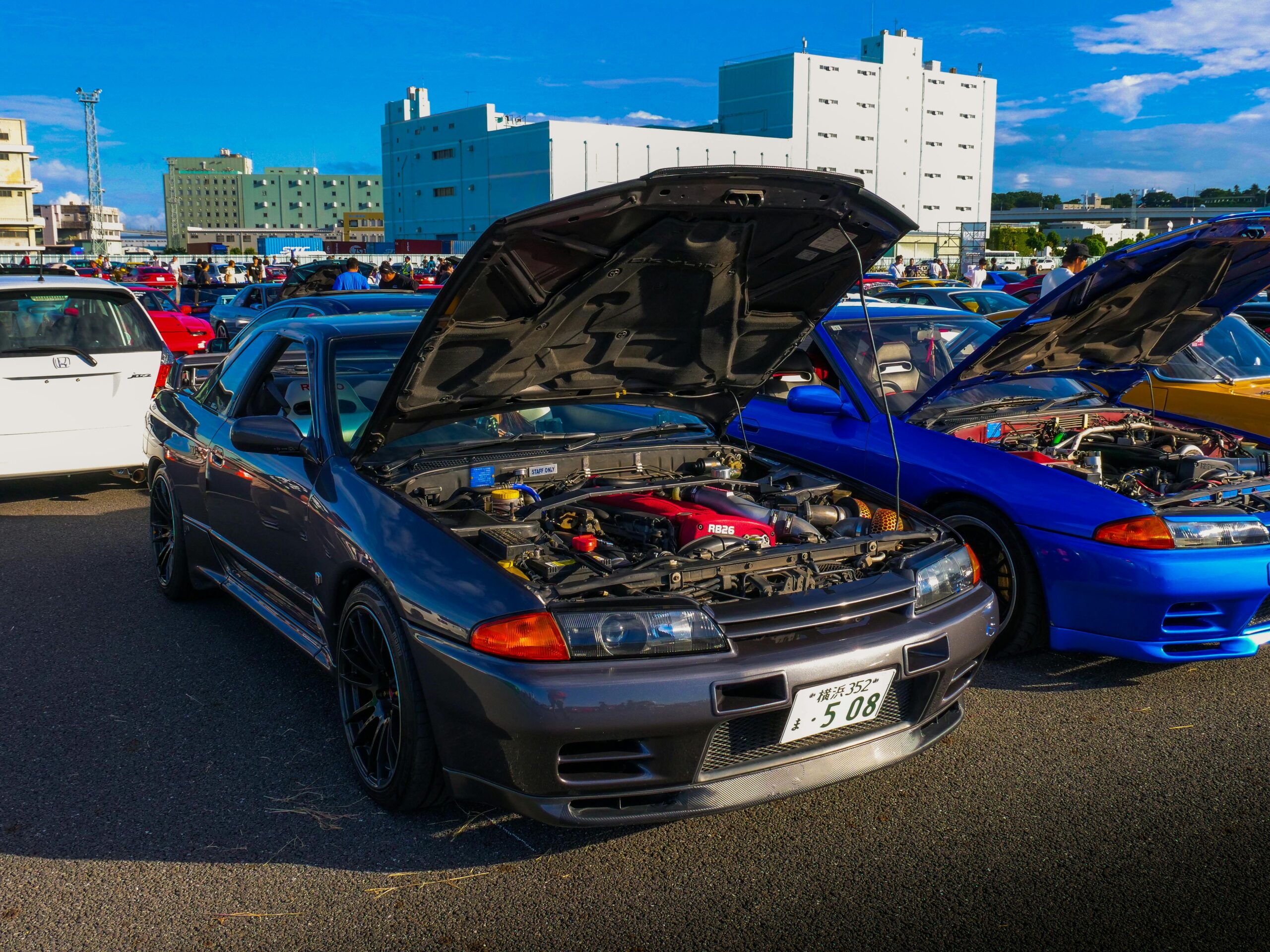 Eine Sammlung klassischer JDM-Autos mit geÃ¶ffneten Motorhauben bei einem Autotreffen im Freien, das die kultige japanische Fahrzeugkultur prÃ¤sentiert.