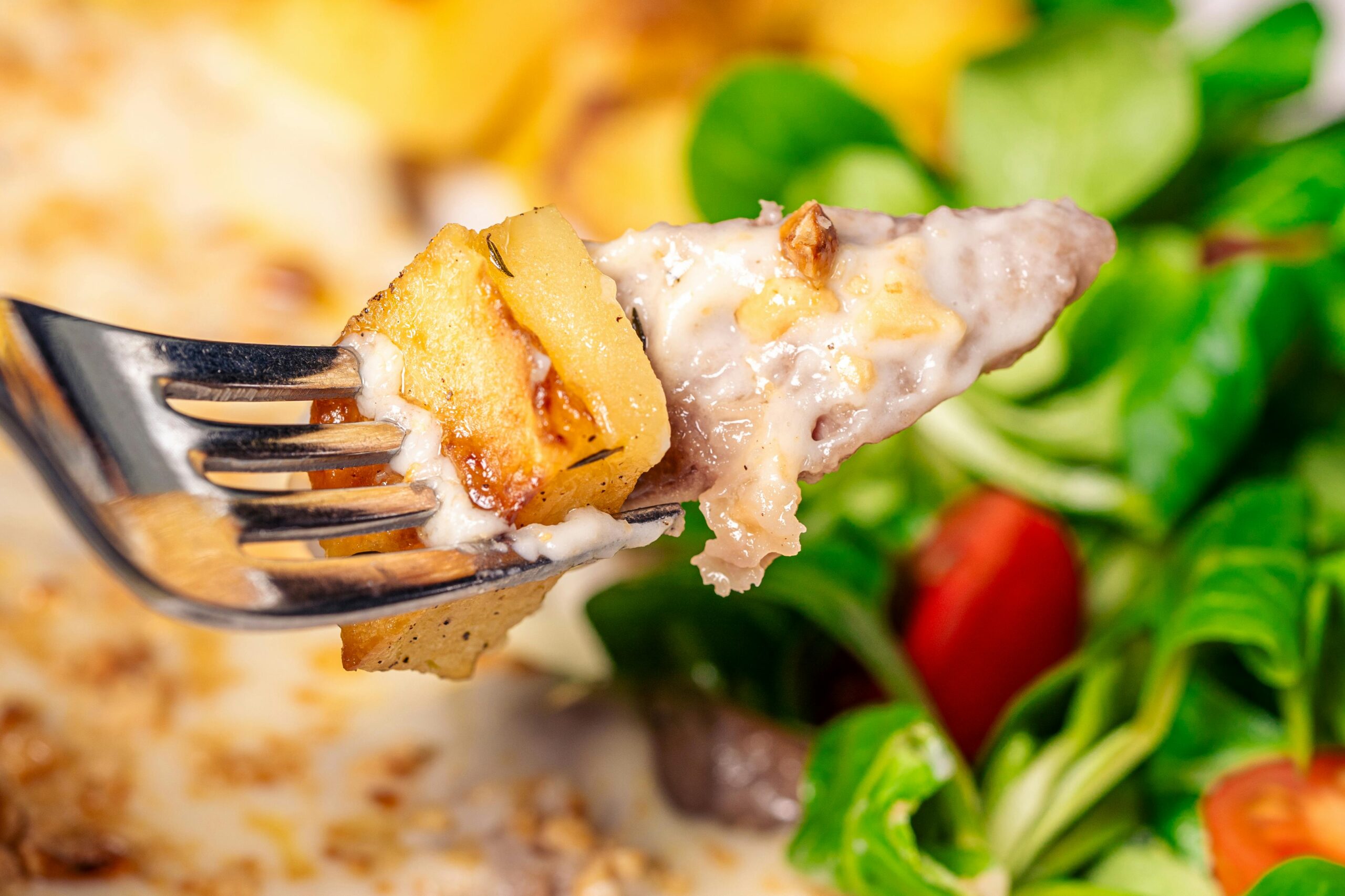 Nahaufnahme einer Gabel, die ein KÃ¤se-Kartoffelgericht mit frischem Salat im Hintergrund hÃ¤lt.