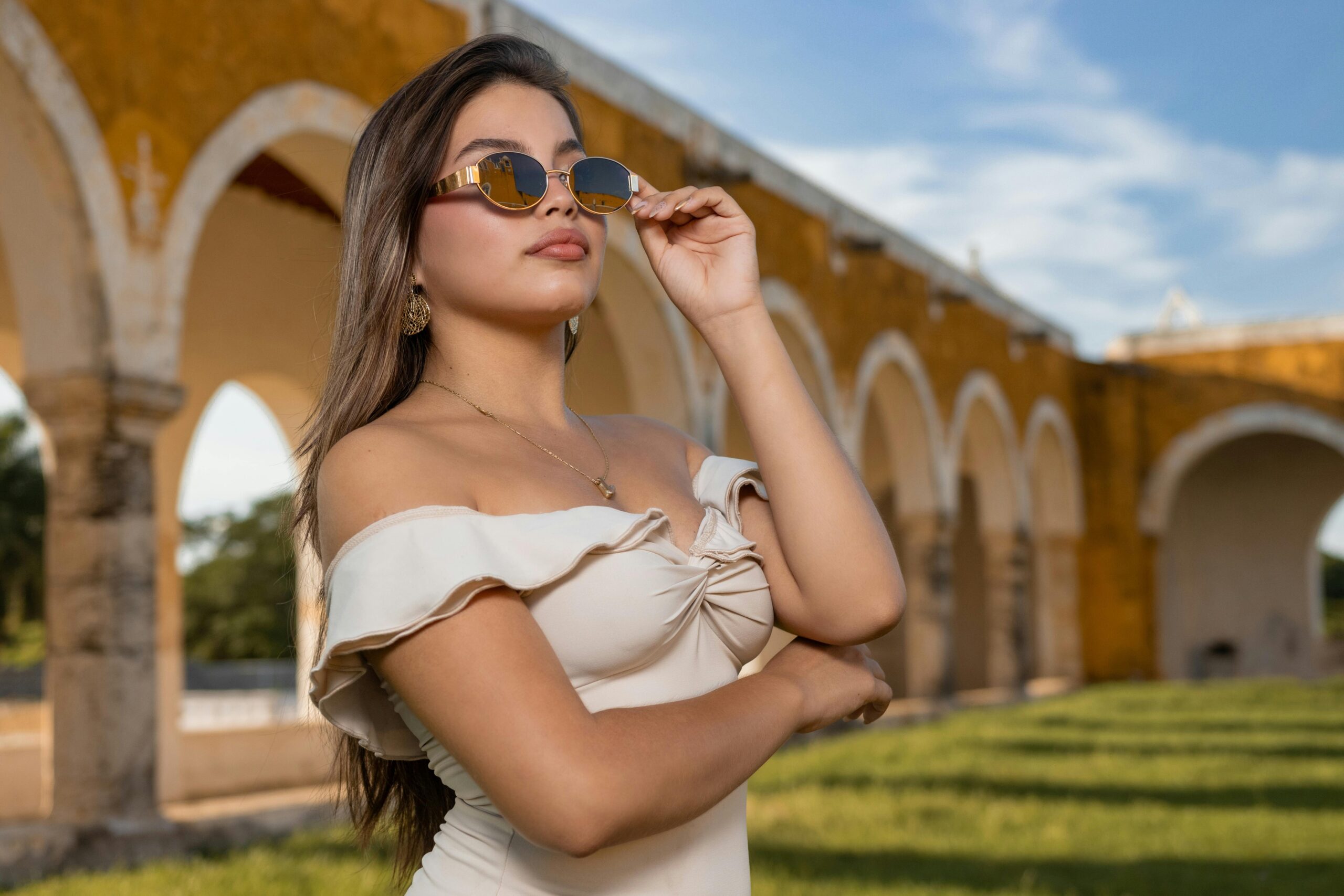 Frau im schulterfreien Kleid posiert mit Sonnenbrille an einer historischen StÃ¤tte mit BÃ¶gen.