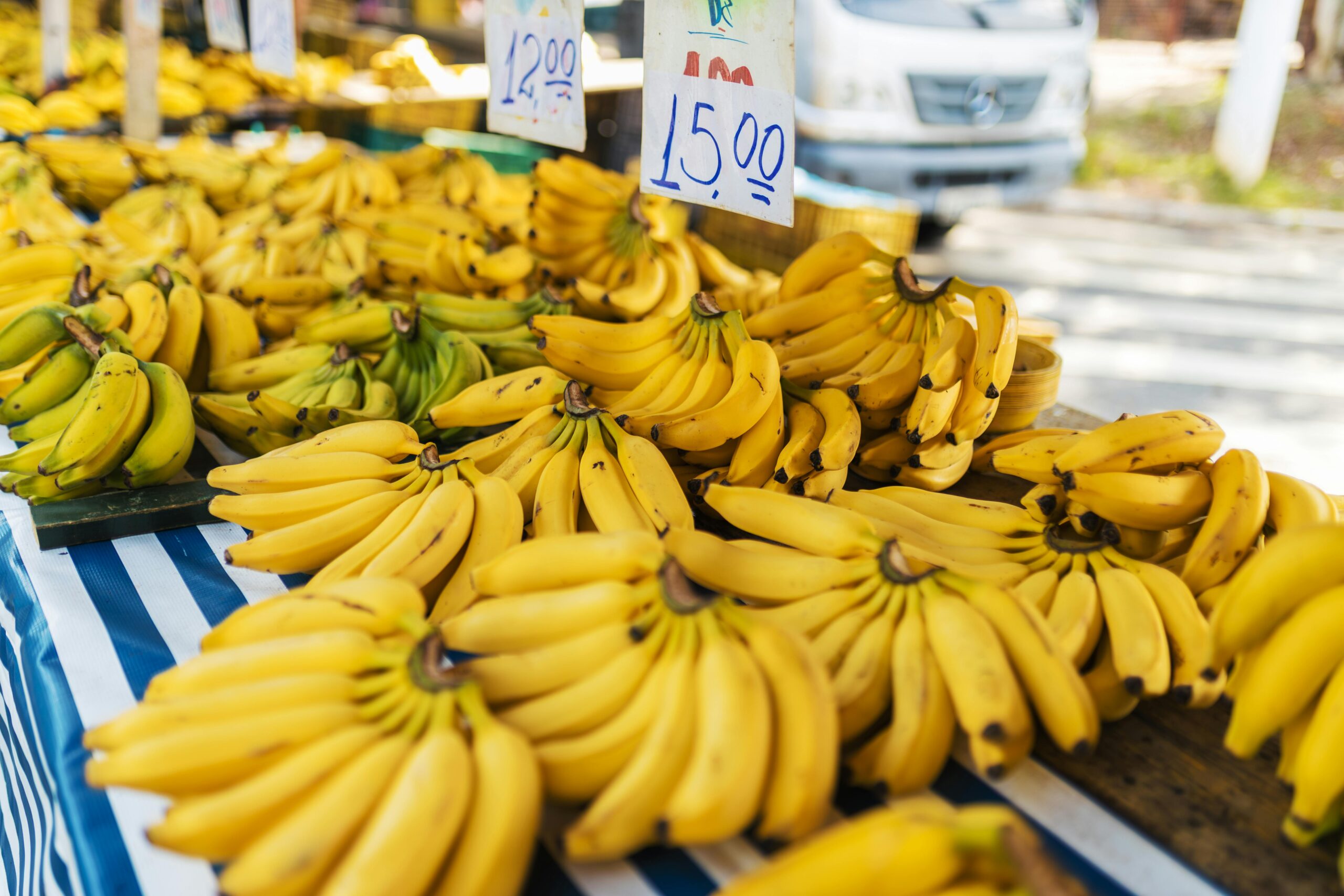 Frische, reife Bananen werden auf einem Freiluftmarkt ausgestellt, Preisschilder sind sichtbar.