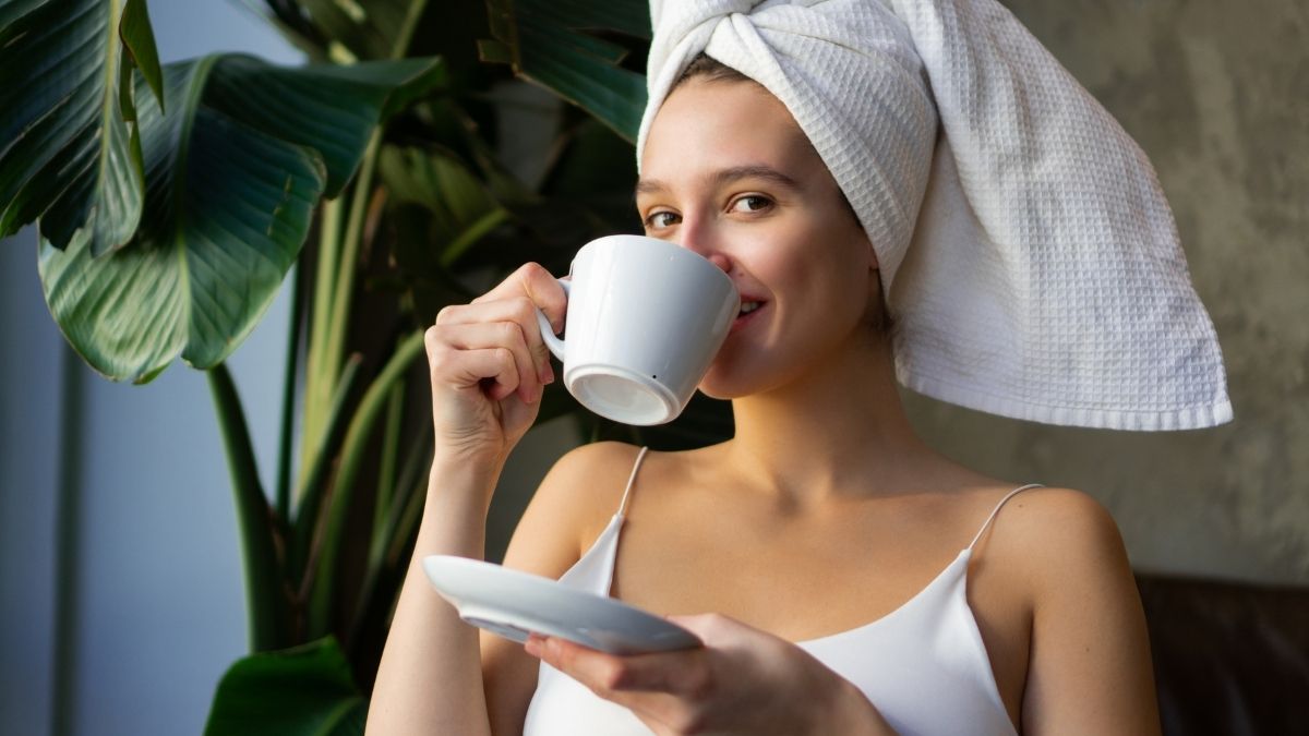 Hübsche Dame mit Badetuch auf dem Kopf bei der Morgenroutine Tee trinken